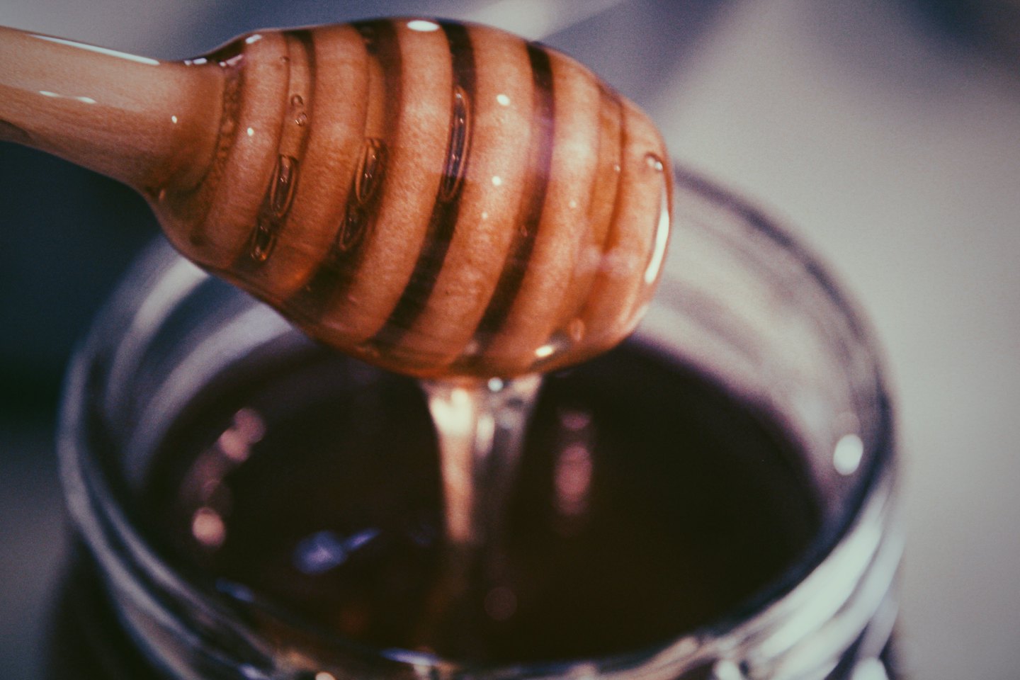 Golden honey drips from a wooden dipper into a jar.